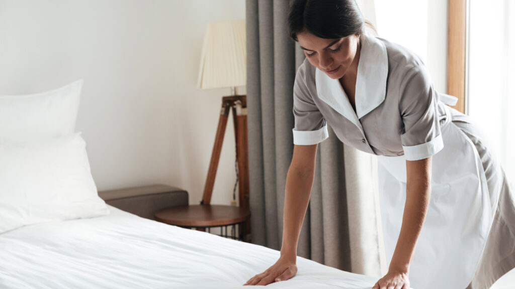 Hotel maid using proper ergonomics to make the bed.